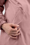 A close-up shot of a person's hand with neatly manicured nails placing or removing an item from the front pocket of a PASTEL PINK WINDBREAKER. The sleeve of The Windbreaker Jacket has elastic at the wrist, adding a touch of stylish clothing to the scene.